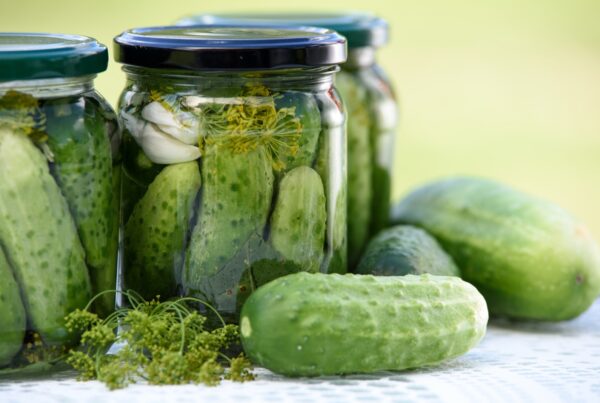 Jars of pickled cucumbers in brine with fresh dill and garlic, beside fresh cucumbers