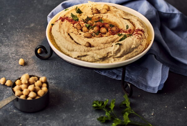 A bowl of hummus garnished with chickpeas, paprika, and fresh parsley, beside a measuring cup of dried chickpeas