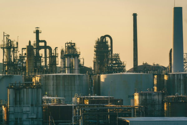 Industrial chemical plant at golden hour with large storage tanks, distillation columns, and process piping