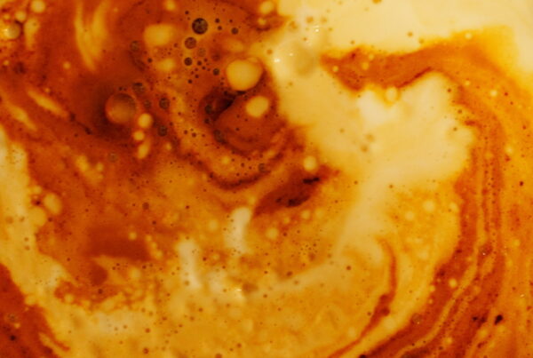 Macro close-up of creamer swirling into black coffee, forming pale marbled ribbons and bubbles