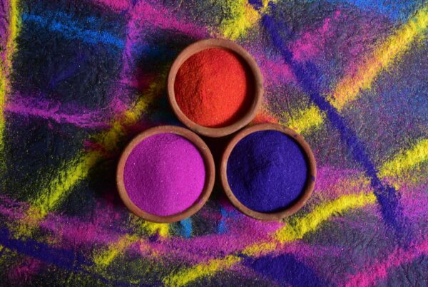 Three clay bowls of red, magenta, and violet color powders on a multicolored background