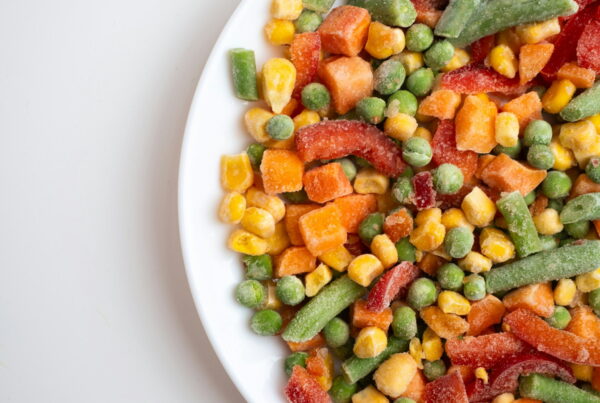 Frost-covered frozen mixed vegetables, including peas, corn, diced carrot, green beans, and red pepper strips, on a white plate